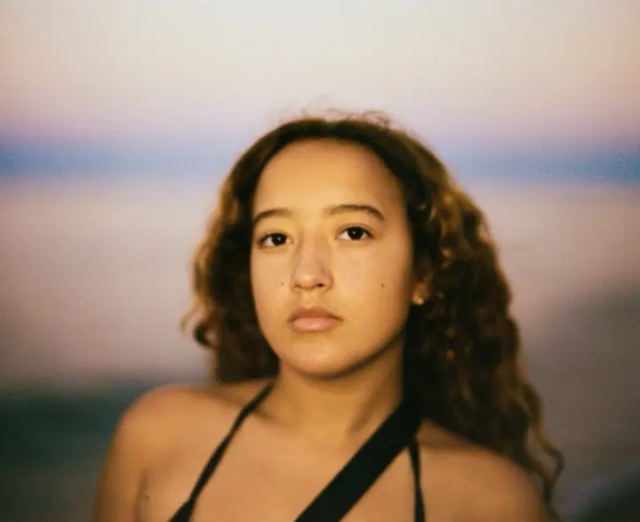 A softly focused colour portrait of a woman against a blue and pink background.