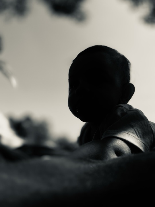 A dark silhouette of a seated child outdoors.
