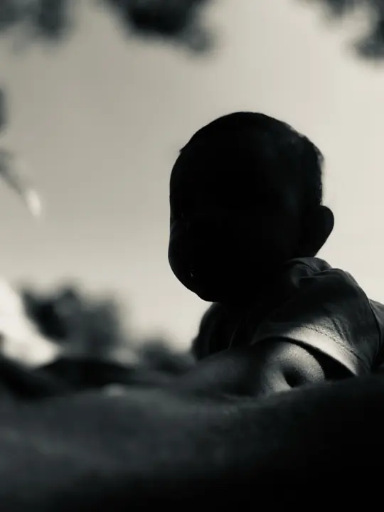 A dark silhouette of a seated child outdoors.