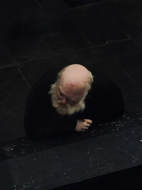 An overhead portrait of an older bearded man leaning on a dark surface.