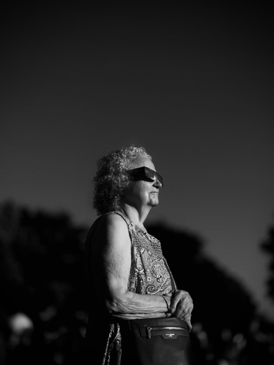 A woman wearing sunglasses and standing in profile, photographed in black and white.
