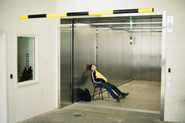A lone seated figure waiting between open lift doors.