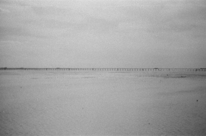 Two distant figures crossing a pale, empty shoreline.