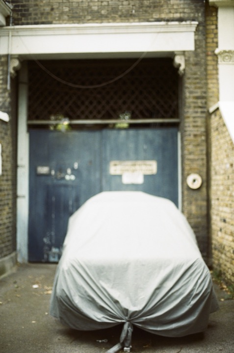 A covered car standing outside closed blue doors.