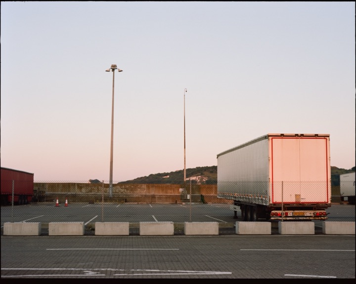 A lone lorry parked beneath tall lights at dusk.