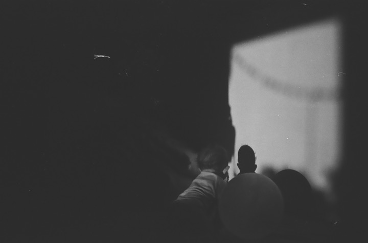 A shadowed crowd facing a bright rectangular window.