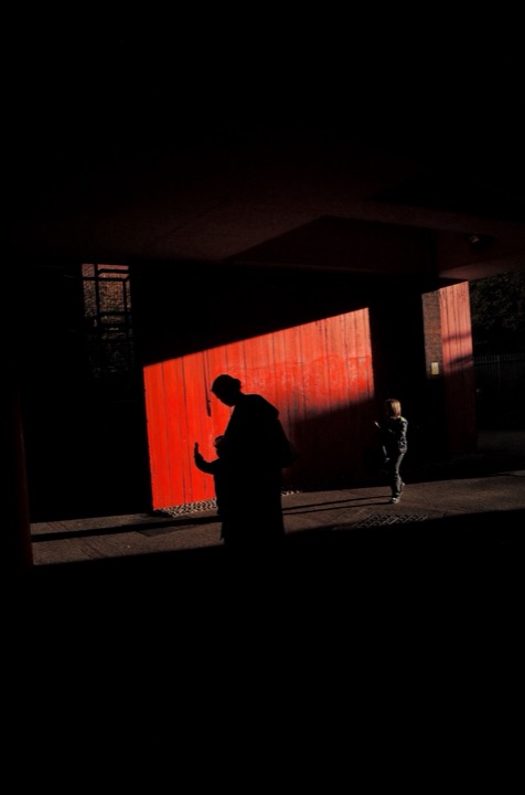 Two silhouettes facing a red-lit screen across a dark room.